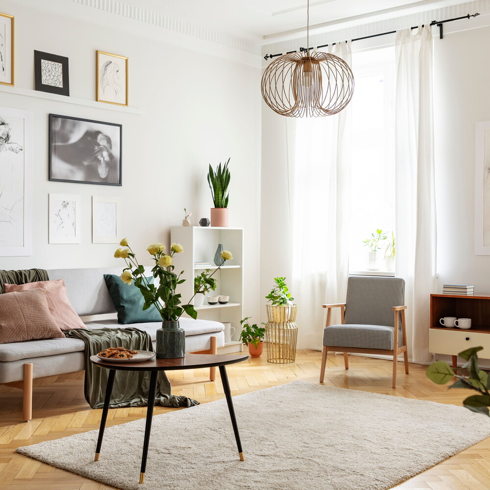 Bright living room with grey sofa, armchair, coffee table with flowers, gallery wall, parquet and indoor plants – modern holiday apartment.